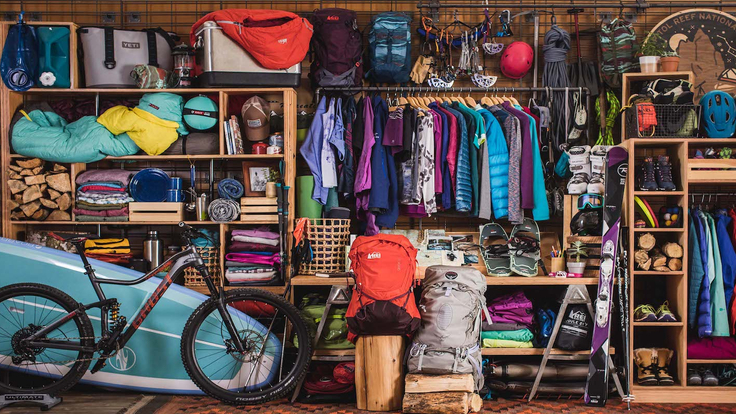 An extensive selection of outdoor gear on shelves and other storage fixtures; a bike and a stand-up paddleboard (SUP)are in the foreground.