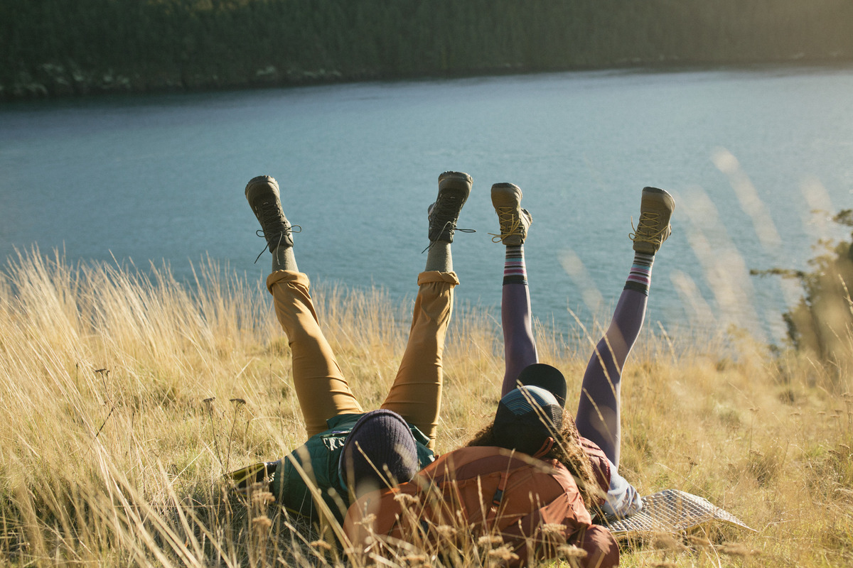 Two people laying on their backs in a field with their feet in the air.