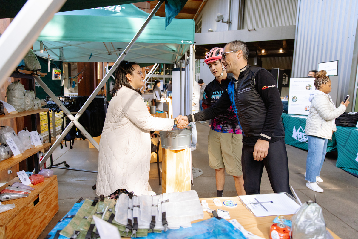 An individual shakes hands with a cyclist at a marketplace.